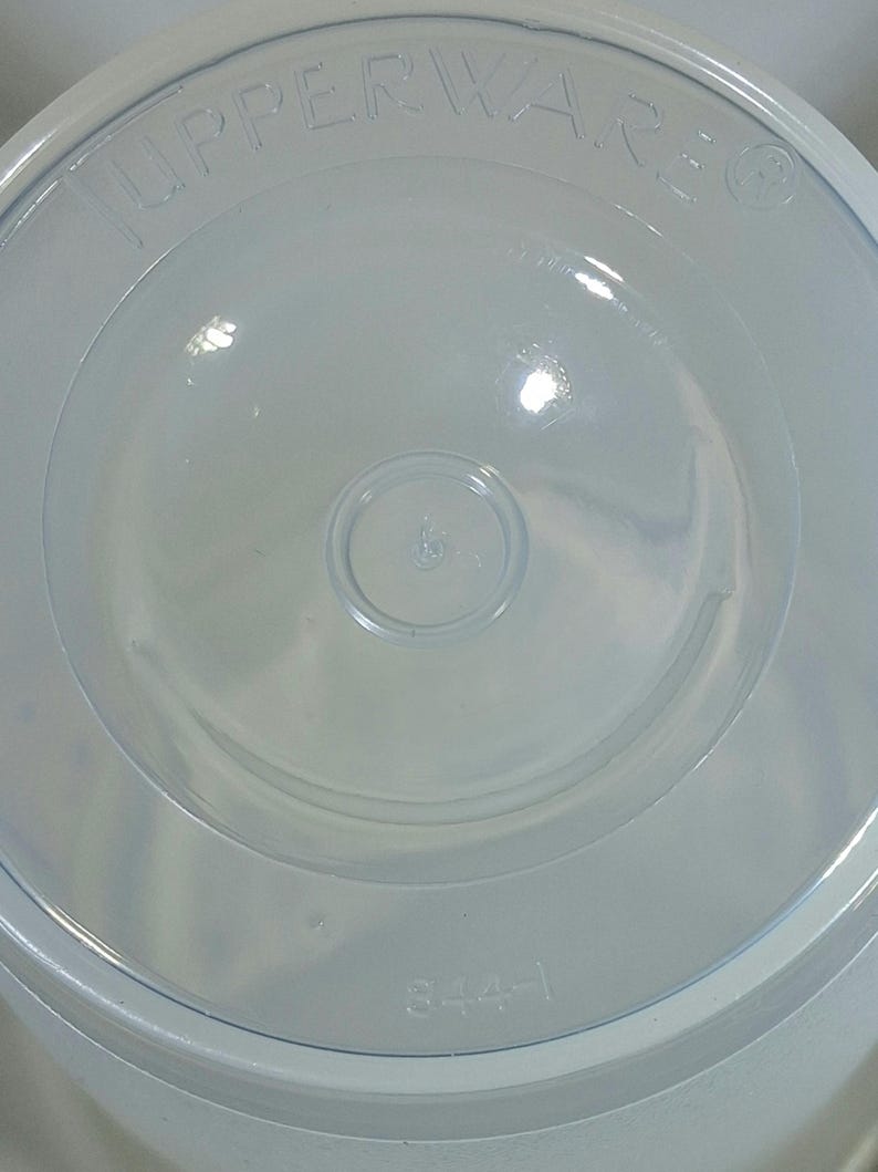 May include: A clear, circular Tupperware lid with the brand name embossed around the edge. The lid has a central circular indentation and the number "6" is visible. The number "344-1" is printed on the lid.