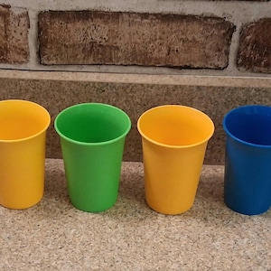 May include: Four colorful plastic cups in yellow, green, yellow, and blue. The cups are arranged in a row, each with a cylindrical shape and a wide opening. The cups are made of a smooth, solid material.