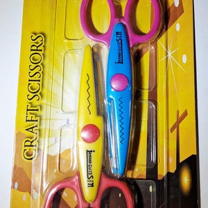 May include: A two-piece set of craft scissors in yellow and blue, packaged on a yellow card labeled Walk With Jesus Collection and Jesus Cuts Sin. The scissors feature pink finger loops and pink center rivets, with zigzag blades for decorative cutting.