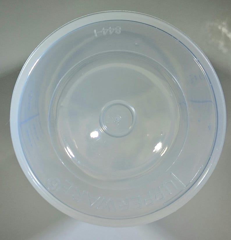 May include: A clear, round plastic container with a slightly flared rim. The container has a circular base and a small, raised circle in the center. The text "844-1" is printed on the rim. The word "TUPPERWARE" is also visible.
