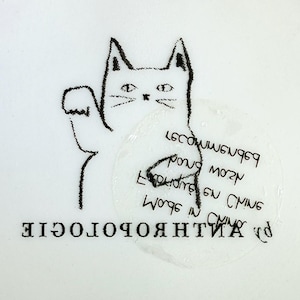 Puede incluir: Ilustraci&oacute;n en blanco y negro de un gato con la pata levantada. El gato est&aacute; dibujado con un estilo sencillo y esbozado. La palabra "ANTHROPOLOGIE" est&aacute; impresa en la parte inferior, y hay texto en un c&iacute;rculo cerca del gato.