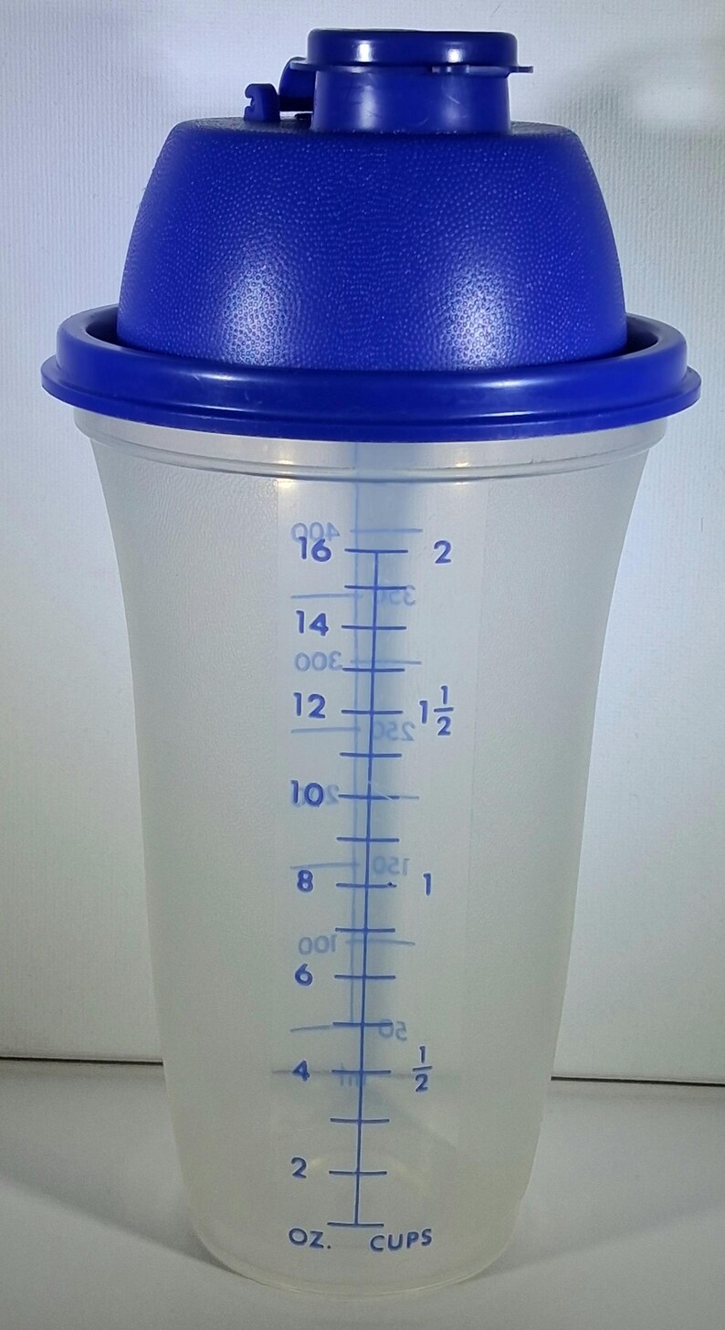 May include: A clear plastic shaker with a blue lid and cap. The shaker has measurement markings in ounces and cups, ranging from 2 to 16 ounces. The blue lid has a textured surface.