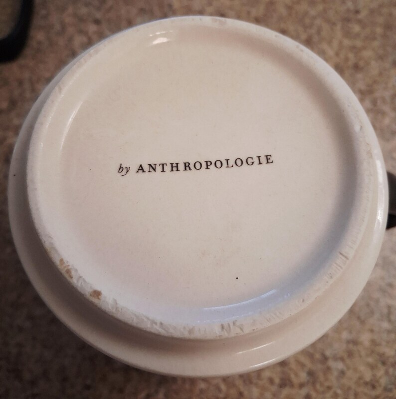 May include: A white ceramic mug with a black handle and the text "But First, Coffee" in a black, bold font. The mug is on a white surface.