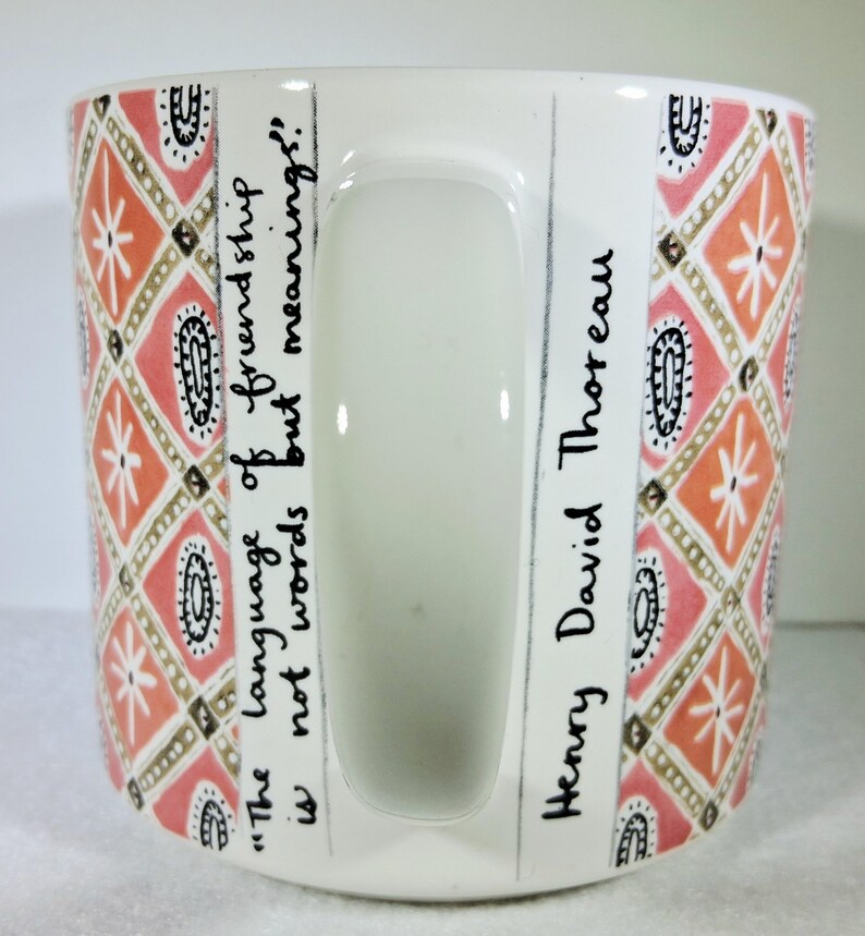 May include: White ceramic mug with a handle, featuring a repeating pattern of orange, pink, and gold geometric shapes. The mug has the quote "The language of friendship is not words but meanings!" and the name "Henry David Thoreau" written on it.