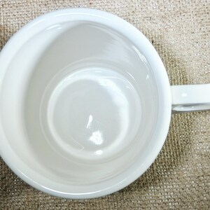 May include: A white ceramic mug, viewed from above, showing the interior and handle. The mug has a simple, clean design with a glossy finish. The handle is a simple loop. The mug is empty.