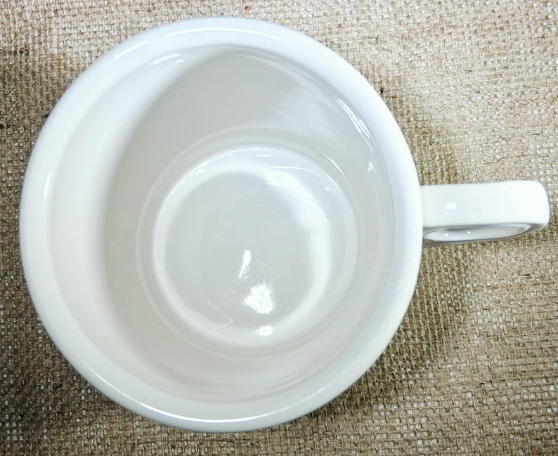 May include: A white ceramic mug, viewed from above, showing the interior and handle. The mug has a simple, clean design with a glossy finish. The handle is a simple loop. The mug is empty.