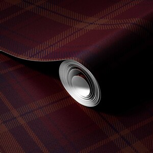 May include: A roll of wallpaper featuring a deep burgundy and dark brown plaid pattern. The design consists of intersecting horizontal and vertical lines forming a classic tartan grid. The roll is partially unspooled, revealing a white interior core.