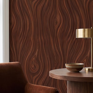 May include: A wall covered in wallpaper featuring a dark brown wood grain pattern with swirling, organic lines. In the foreground, a brown velvet armchair sits next to a round wooden pedestal table holding a small ceramic bowl and a brass lamp.