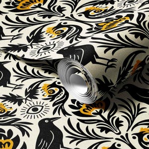May include: Wallpaper roll featuring a repeating pattern of black birds, flowers, and eye motifs on an off-white background. The design includes yellow accents and stylized floral elements. The roll is partially unrolled, revealing the pattern.