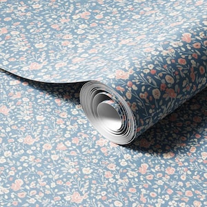 May include: A roll of wallpaper featuring a repeating pattern of small, light pink and white flowers with green leaves on a dusty blue background. The paper is partially unrolled, revealing the cylindrical core and the continuous floral print.