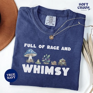 以下が含まれることがあります： 「FULL OF RAGE AND WHIMSY」の文字と、キノコ、カタツムリ、馬車の気まぐれなグラフィックが特徴の、トゥルーネイビーのTシャツ。「TRUE NAVY」の文字とComfort Colorsのタグも付いています。