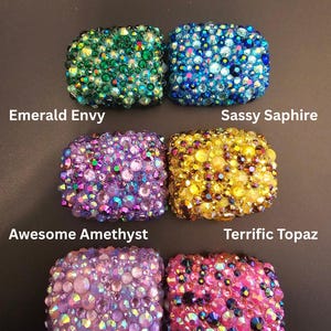 Może przedstawiać: Sześć prostokątnych przedmiotów pokrytych kamieniami szlachetnymi. U góry znajduje się napis "The Gemstone Collection". Obiekty są oznaczone jako "Emerald Envy", "Sassy Saphire", "Awesome Amethyst", "Terrific Topaz", "Quirky Quartz" i "Tenacious Tourmaline".