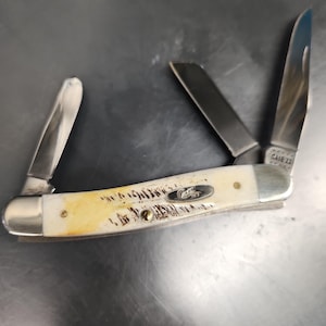May include: A multi-blade pocket knife featuring a cream-colored handle with brown textured markings and a silver metal bolster. The handle displays a silver oval inlay with the word Case. Three stainless steel blades are extended at various angles.