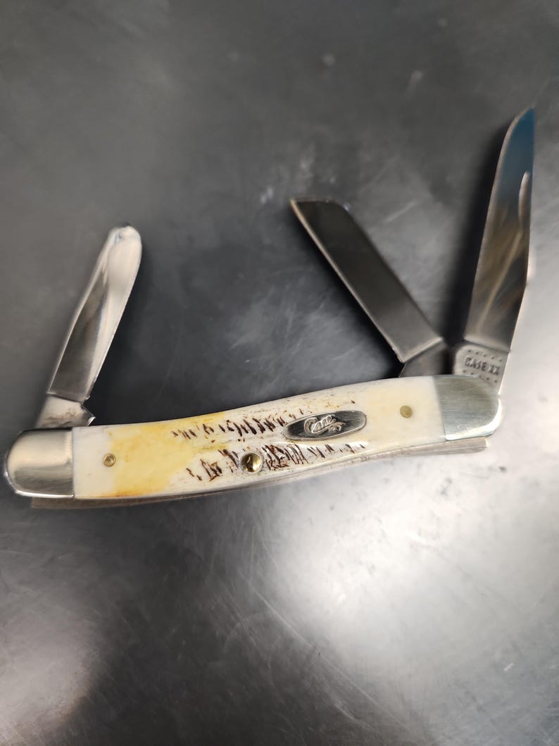 May include: A multi-blade pocket knife featuring a cream-colored handle with brown textured markings and a silver metal bolster. The handle displays a silver oval inlay with the word Case. Three stainless steel blades are extended at various angles.