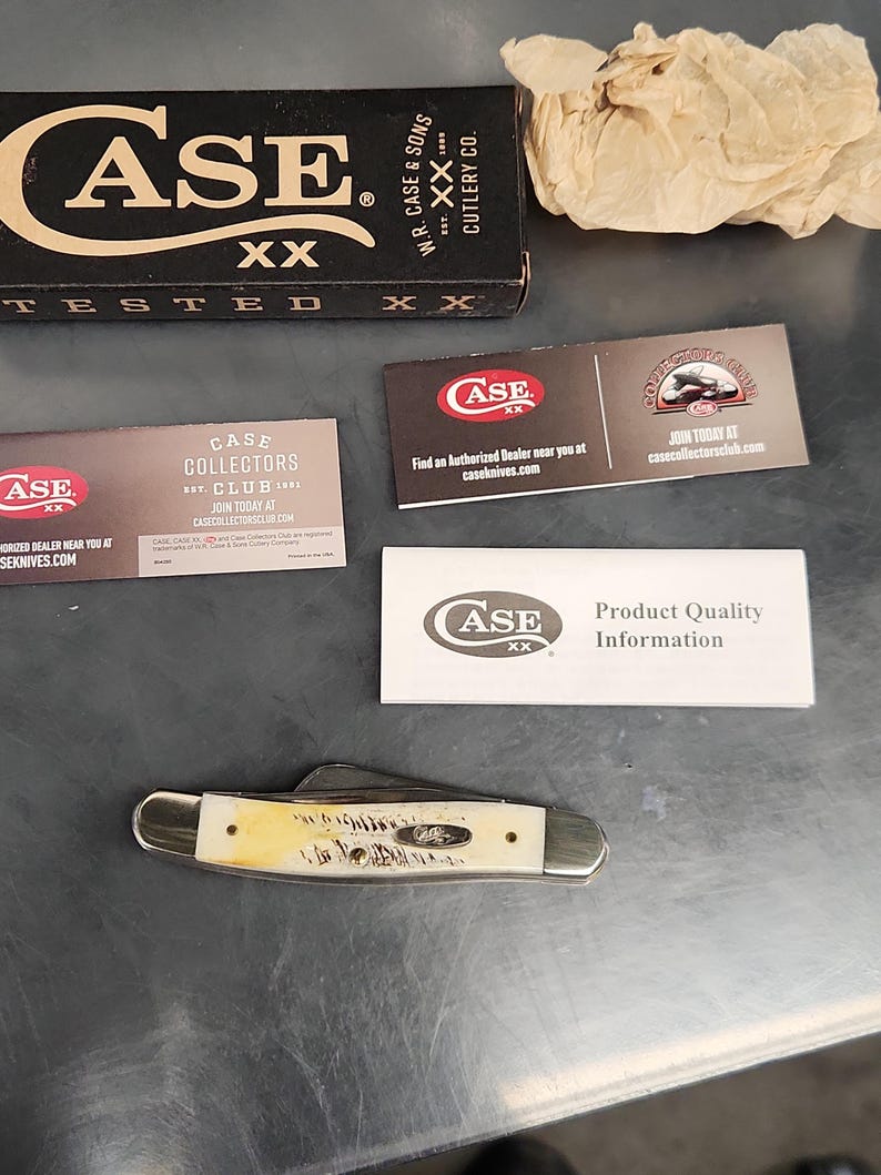 May include: A folding pocket knife with a cream-colored handle featuring a textured finish and silver metal bolsters. The set includes a black Case XX branded box, a piece of crumpled tan paper, and three informational cards with Case XX branding.