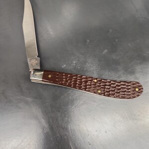 May include: A folding pocket knife with a single silver-toned steel blade and a dark brown handle featuring a textured, reptilian-like pattern. The handle is secured with three small brass-colored rivets and a polished silver bolster near the blade.
