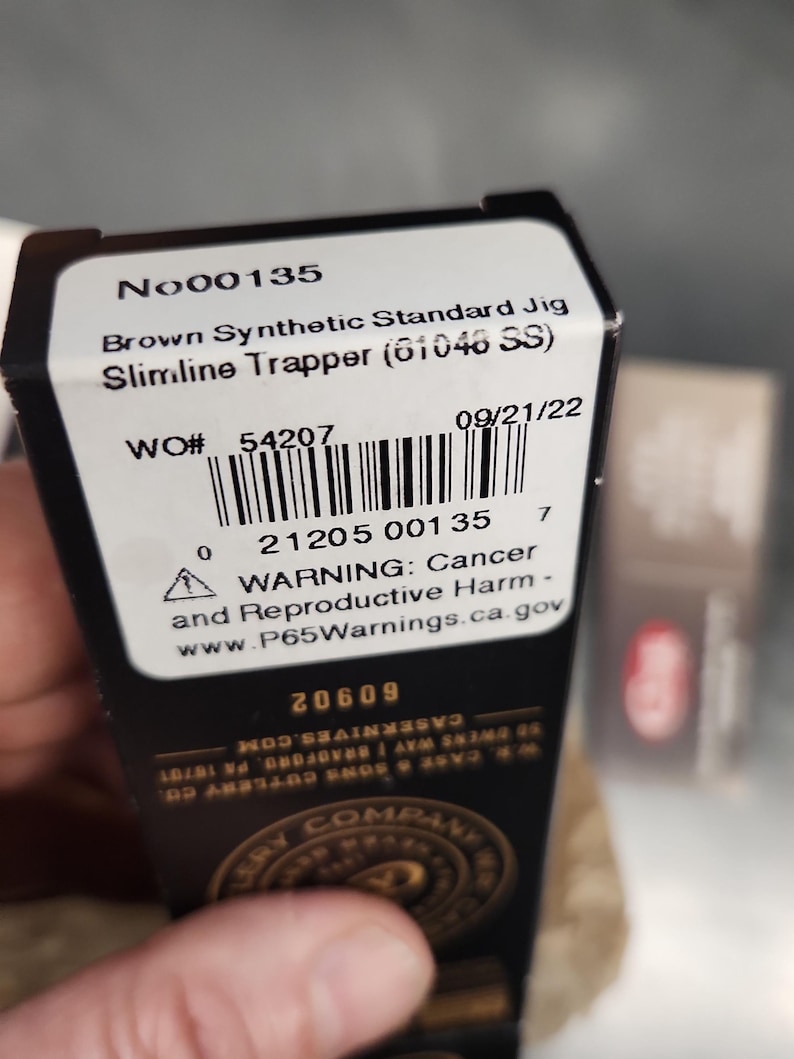 May include: A black rectangular product box with a white label featuring the text No00135, Brown Synthetic Standard Jig Slimline Trapper (61046 SS), a barcode, and a warning regarding cancer and reproductive harm with the website P65Warnings.ca.gov.