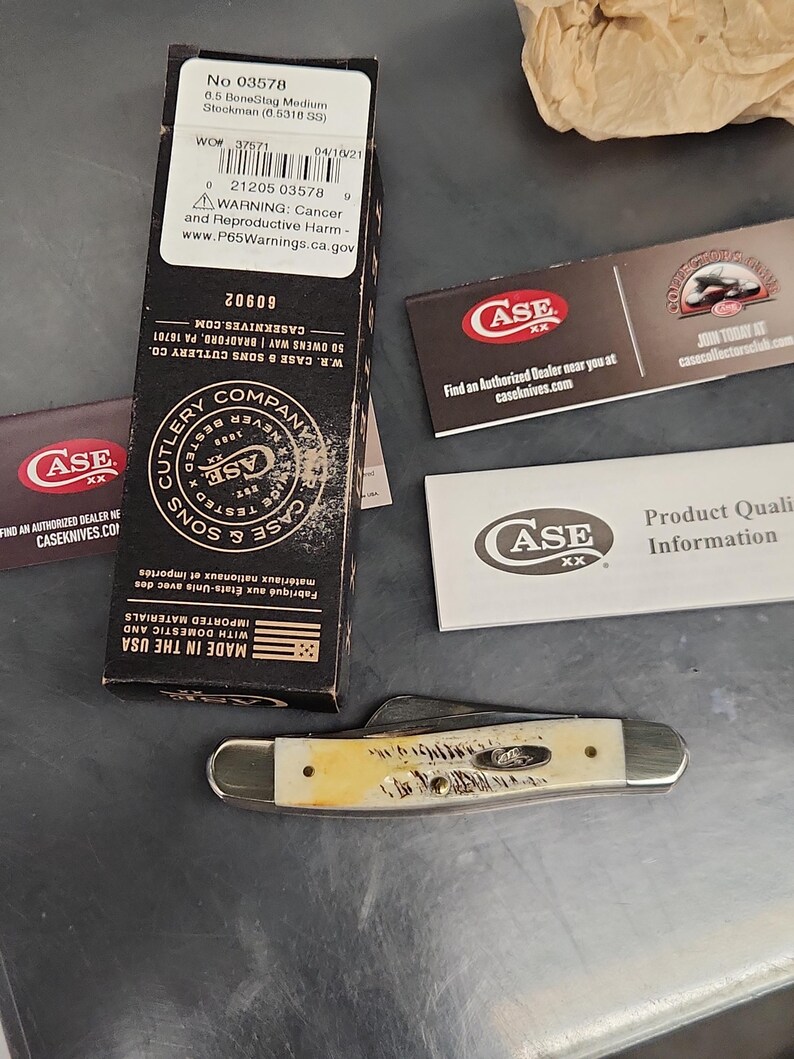 May include: A folding pocket knife with a textured cream-colored handle and silver metal bolsters, accompanied by its original black cardboard packaging box, a Case XX brand information card, and a collector club promotional insert.
