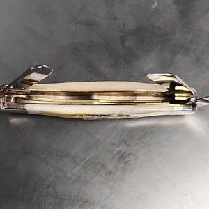 May include: A folding pocket knife with an off-white handle and metallic silver bolsters. The knife features multiple partially extended steel blades and internal brass liners visible between the handle scales, showing a multi-tool construction.