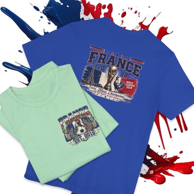 May include: A royal blue t-shirt featuring a graphic of the Eiffel Tower, a soccer trophy, and a rooster with the text FRANCE 2018 WORLD CHAMPIONS. A light green t-shirt with a smaller graphic of a rooster, a soccer ball, and FRANCE EST. 2018.