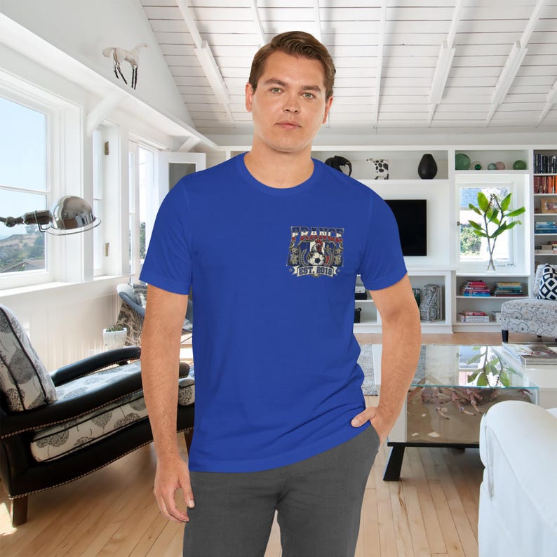 May include: A royal blue short-sleeve t-shirt featuring a small graphic on the left chest. The design includes a soccer ball, laurel wreaths, and the text "FRANCE" and "EST. 2019" in white and red lettering against a blue and white background.