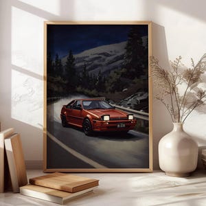 May include: Framed art print featuring a red sports car driving on a winding mountain road. The artwork depicts a nighttime scene with a dark blue sky, snow-capped mountains, and evergreen trees. The car has black wheels and a license plate.