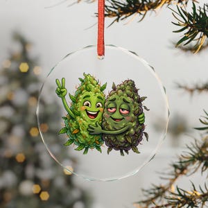 May include: A clear, round Christmas ornament with a red ribbon. The ornament features a cartoon illustration of two green cannabis buds hugging. One bud is giving a peace sign, and the other has red eyes.
