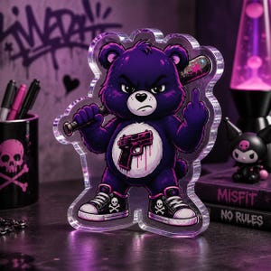 Peut inclure: Figurine en acrylique violet représentant un ours en colère, tenant une batte de baseball et faisant un doigt d'honneur. L'ours porte des baskets avec des têtes de mort. L'ours a un dessin de pistolet sur le ventre.