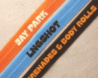May include: Three strips of elastic ribbon in orange, light blue, and black. The orange ribbon features the white text JAY PARK. The light blue ribbon features the black text LNGSHOT. The black ribbon features the orange text SERENADES & BODY ROLLS.