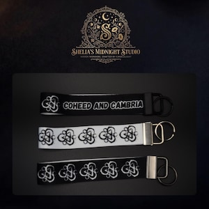 May include: Three keychains with black and white designs. One black keychain has the text "COHEED AND CAMBRIA" in white. The other two keychains have a repeating white design on black and white backgrounds. Each keychain has a metal ring.