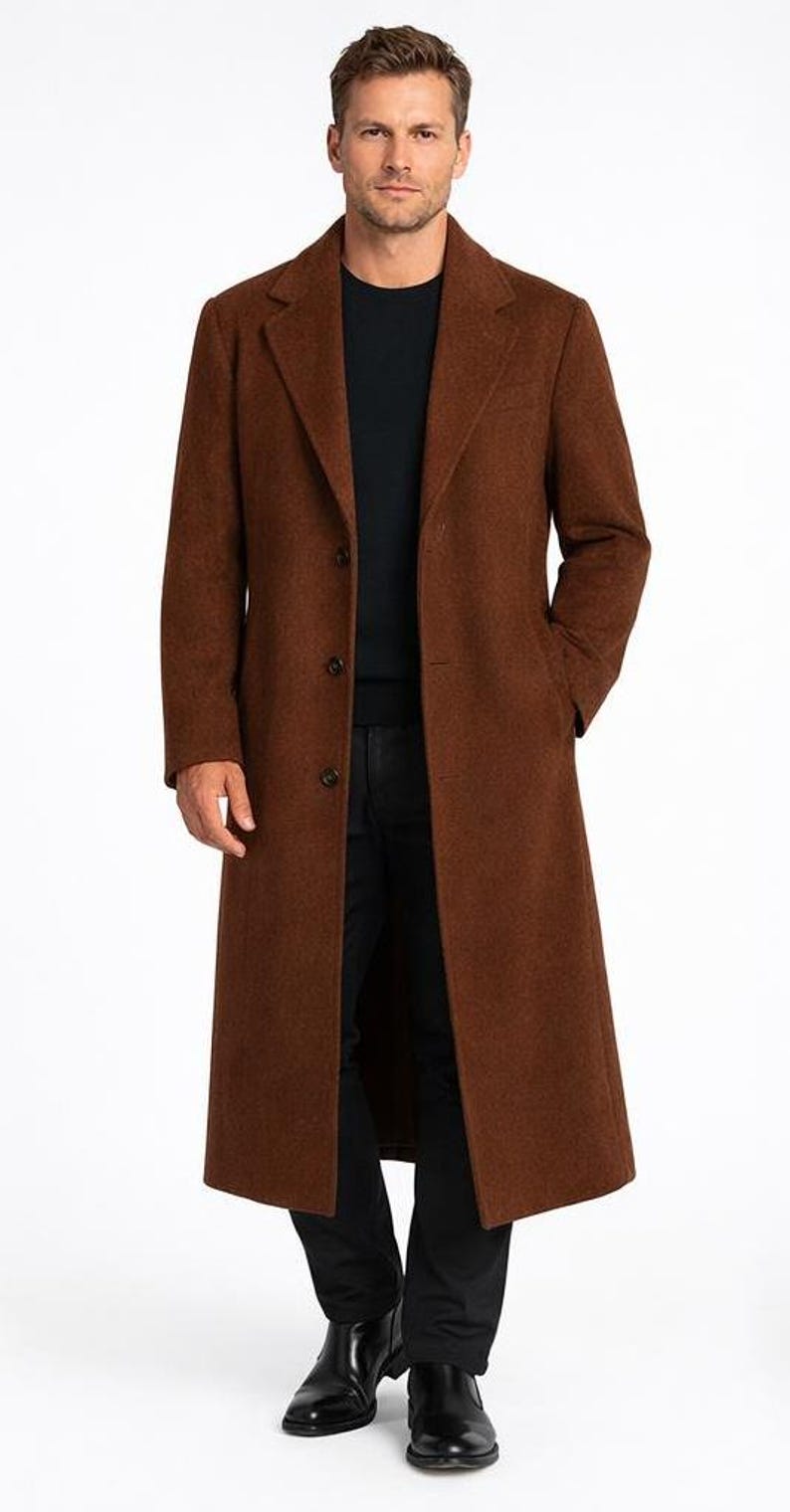 May include: A long, brown overcoat with a classic design. The coat features a notched lapel, three-button closure, and front pockets. The person is wearing a black shirt and black pants.