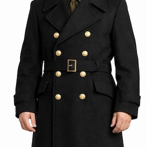 May include: A black double-breasted wool overcoat featuring gold-toned buttons, a matching waist belt with a rectangular buckle, and wide lapels. The coat is worn over an olive green collared shirt with a tie and a black garrison cap.