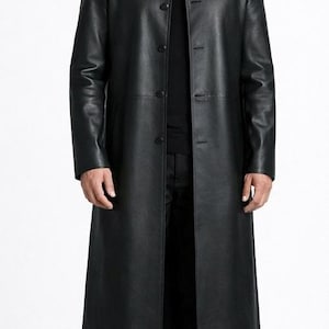 May include: A long, black leather coat with a button-up front. The coat reaches to the ankles and has a classic, tailored design. The model is wearing black pants and black boots. The coat is a sleek and stylish outerwear piece.