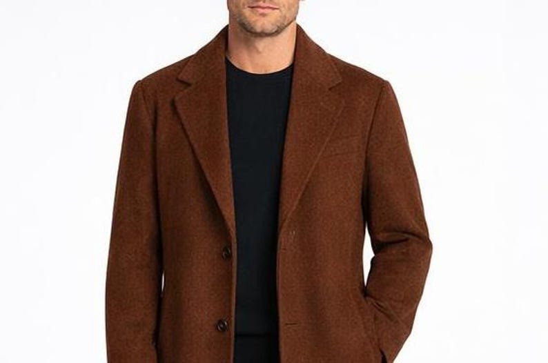 May include: A brown wool coat with a notched lapel and two-button closure. The coat is worn over a black crew neck shirt. The coat has a classic, tailored design.