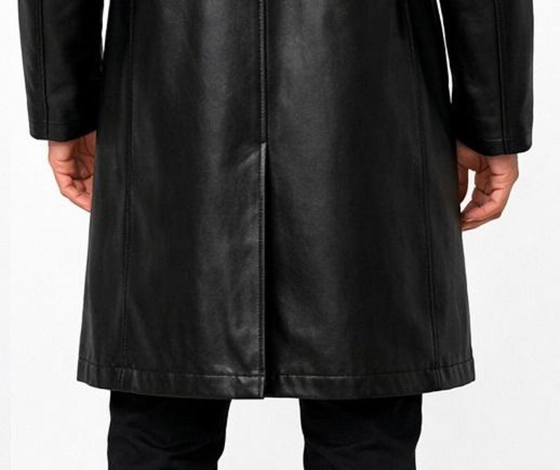 May include: A black leather coat with a classic design. The coat features a long length, a tailored fit, and visible stitching details. The image shows the back of the coat, highlighting the seams and the split at the bottom.