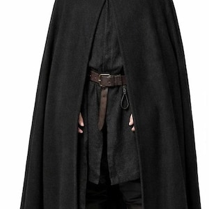 May include: A black hooded cloak with a gold clasp, worn over a dark tunic and brown leather belt. The cloak is made of a heavy fabric, and the outfit is completed with dark boots. The overall style suggests a medieval or fantasy theme.