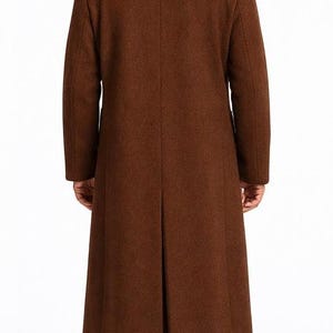 May include: A long, brown overcoat with a classic design. The coat is made of a textured fabric and features a notched collar and a single vent in the back. The coat is worn over black pants and shoes.