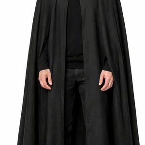 以下が含まれることがあります： ハイカラーとシングルボタン留めの長い黒いケープ。ケープは流れるような生地で作られており、黒い服装の上に着用されています。全体的な外観はゴシックで劇的です。
