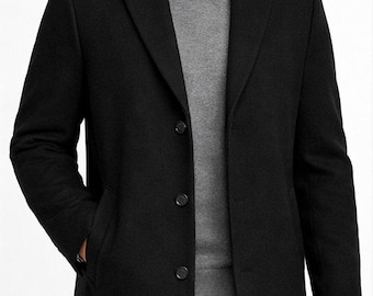 May include: A black overcoat with a notched lapel and three-button closure. The coat is worn over a gray sweater and a white collared shirt. The model is wearing black pants.
