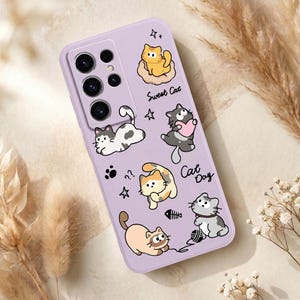 May include: A lavender phone case featuring cartoon cats and the phrases "Sweet Cat" and "Cat Day." The case has a series of camera lenses and a collection of playful cat illustrations, including a cat with a heart and a cat playing with yarn.