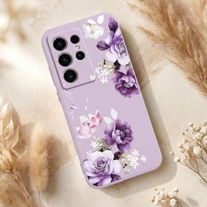 Puede incluir: Una funda de teléfono lavanda adornada con un diseño floral. La funda presenta un grupo de flores moradas, blancas y rosas. La funda del teléfono tiene un recorte para la cámara y botones.
