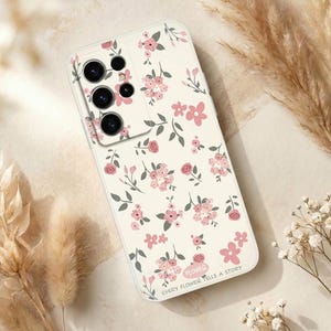 Puede incluir: Una funda de teléfono blanca con un estampado floral de flores rosas y hojas verdes. La funda tiene un recorte para la cámara y el texto "EVERY FLOWER TELLS A STORY". El diseño se repite.
