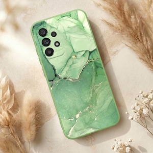 May include: A green phone case with a marble design. The case features shades of green with gold accents. The phone case has a camera cutout and button placements.
