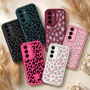 May include: A selection of mobile phone cases featuring leopard print patterns in various colours. The cases include black, teal, burgundy, pink, and white. Each case has a camera aperture and a protective bumper. The cases are displayed on a neutral background.