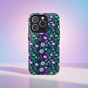 Puede incluir: Una funda de teléfono inteligente con un estampado floral. La funda presenta un fondo oscuro con un diseño repetido de hojas verdes, flores rosas y acentos morados. La funda tiene un acabado brillante y un recorte para la cámara.