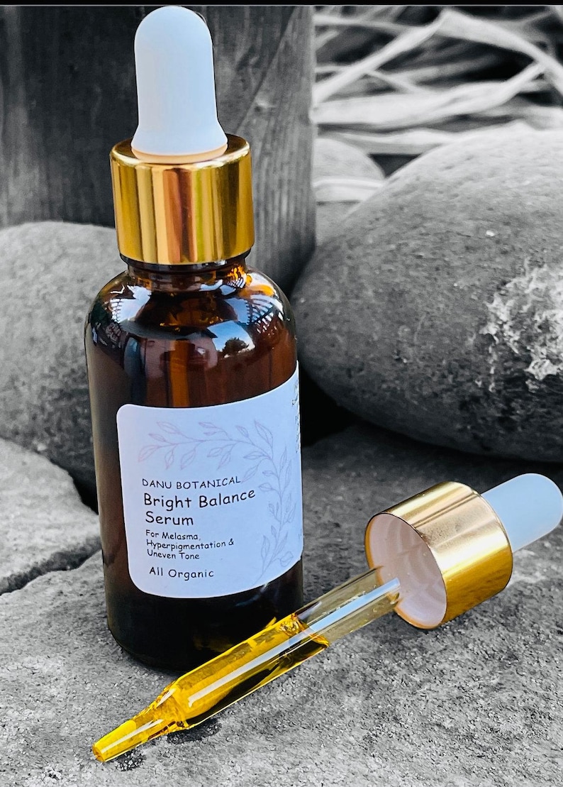 May include: A brown glass bottle of Danu Botanical Bright Balance Serum with a gold dropper. The label indicates the serum is for melasma, hyperpigmentation, and uneven tone. The dropper is filled with a yellow liquid.