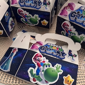party gable white boxes with handles, decorated with Super Mario Galaxy  theme. includes stickers. The boxes feature images of Mario and Yoshi, along with other characters and the game's logo. The background is a dark blue space galaxy  scene. ships fast. can ship multiple boxes together