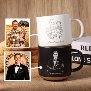 May include: Two ceramic mugs, one white and one black, stacked on top of each other. The white mug features a sketch of a man holding a child, with the text "Alan & Daddy." The black mug has a sketch of a man in a tuxedo, with the name "Vincent."