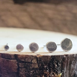 Peut inclure: Cinq boucles d'oreilles en argent de tailles variées sont présentées en rangée. Les boucles d'oreilles ont un aspect martelé et texturé, sur un fond en bois naturel. Les clous d'oreilles varient de petite à moyenne taille.