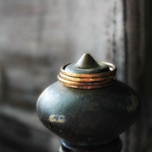 Peut inclure: Gros plan sur un objet décoratif vert foncé avec un sommet conique. Plusieurs fines bagues dorées entourent le sommet. L'objet a une base arrondie et semble être en métal. L'arrière-plan est flou, avec des tons neutres.